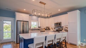 Una cocina moderna con una isla central, armarios blancos, electrodomésticos de acero inoxidable y una lámpara colgante.