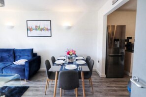 A modern dining area with a blue sofa, a table set for four, and a refrigerator in the background. - Blue Apartment in Peterborough (Peterborough)