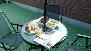 A round glass table with a newspaper, a croissant, a glass of orange juice, and a bowl of grapes. - Blue Apartment in Peterborough (Peterborough)