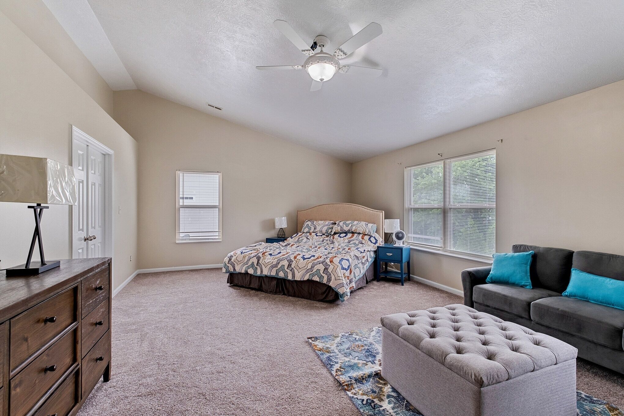 A bedroom with a bed, dresser, nightstands, a gray couch, and a ceiling fan.