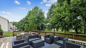 Une terrasse dotée de mobilier d’extérieur, d’une rambarde en bois et offrant une vue sur un espace verdoyant avec des arbres.