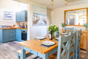 A modern kitchen with blue cabinets, a wooden dining table set for four, and a large mirror above the table.