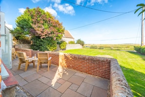 A patio with a brick wall, a wooden table, and two chairs. - Eastgate Cottage and Hideaway, Salthouse, Norfolk (Salthouse)