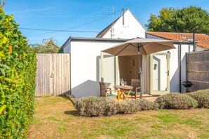 A patio with a table and chairs, a wooden fence, and a white building with a tiled roof.
