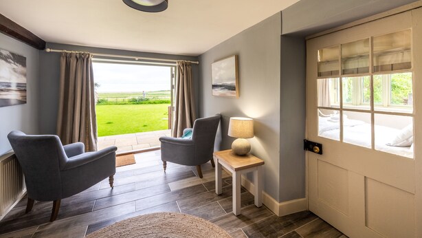 A room with two armchairs, a small table with a lamp, a door with a view, and a painting on the wall. - Eastgate Cottage and Hideaway, Salthouse, Norfolk (Salthouse)