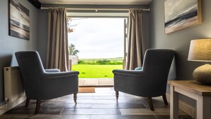 A room with two armchairs facing a sliding glass door leading to a garden. - Eastgate Cottage and Hideaway, Salthouse, Norfolk (Salthouse)