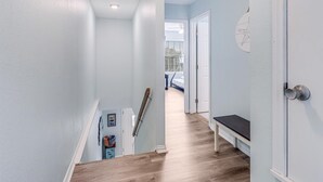 Un pasillo estrecho con paredes azul claro, una escalera de madera y un banco.