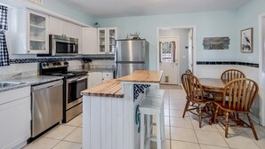 Cocina moderna con armarios blancos, electrodomésticos de acero inoxidable, una isla de madera y un comedor con sillas de madera.