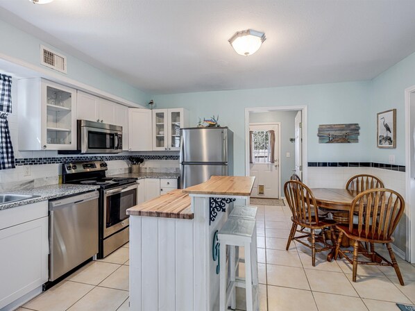 A modern kitchen with white cabinets, stainless steel appliances, a wooden island, and a dining area with wooden chairs.