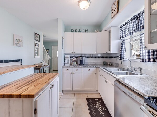 Una cocina con armarios blancos, encimera de madera, estación de café y salpicadero con un letrero de temática playera.
