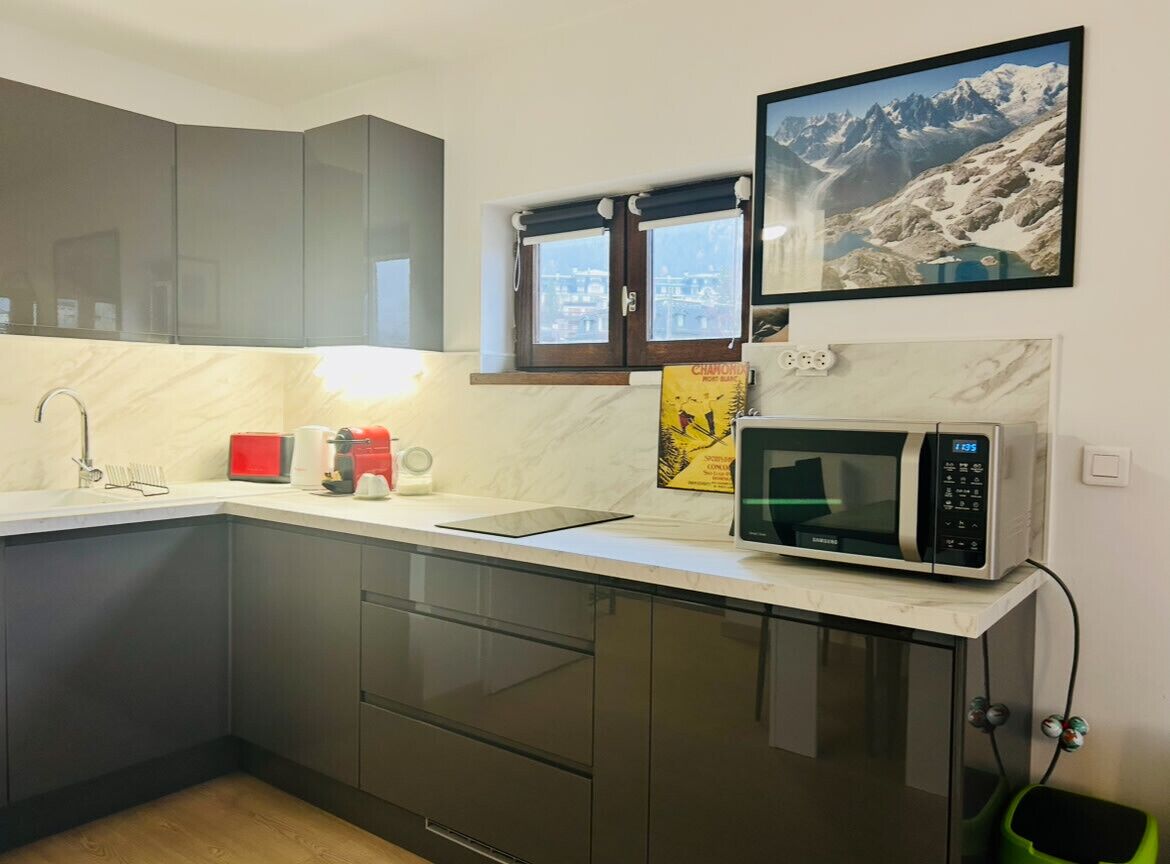 A modern kitchen with dark cabinets, a microwave, and a window with a view of mountains.