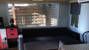 Ett rum med trägolv, en svart soffa, ett matbord med en duk med prickmönster, ett fönster med utsikt över ett trästaket och en röd förvaringsenhet med en skylt.