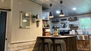 A rustic kitchen with a wooden bar, pendant lights, and a 'KITCHEN' sign.