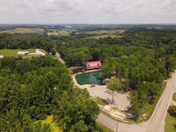 An aerial view of a rural property with a pond, a red-roofed building, and a road.