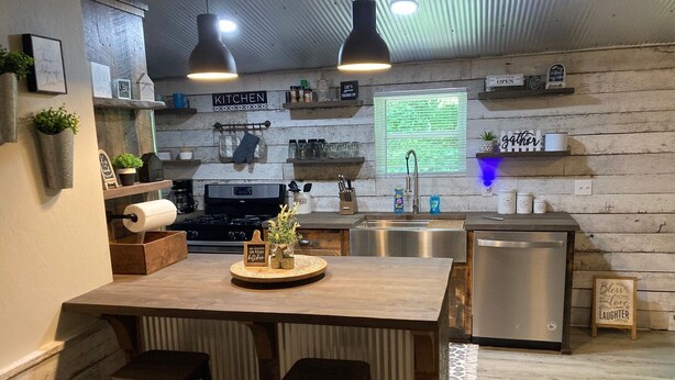 A kitchen with a central island, bar stools, a stove, and a dishwasher.