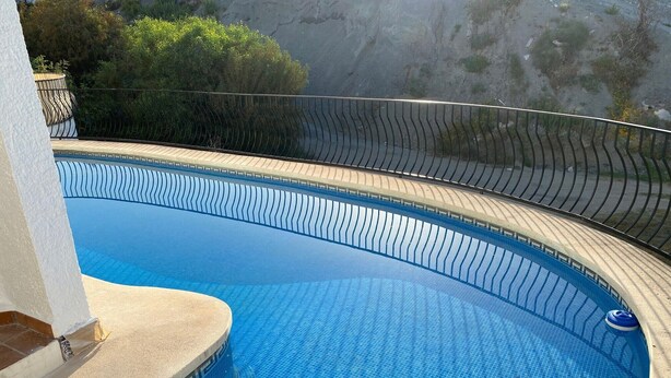 Una piscina curvo con bordo piastrellato, circondata da un solarium a forma di curva e una ringhiera in metallo.