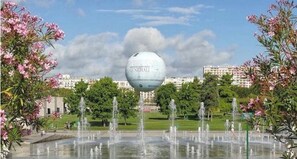 A fountain with multiple water jets in a park setting, surrounded by trees and buildings. - Location 31 Juillet au 15 Aout (Paris)