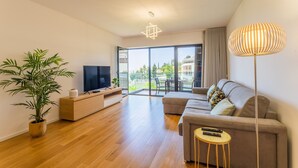 Ein modernes Wohnzimmer mit Sofa, Fernseher, Holzboden, Topfpflanze und einem Balkon mit Aussicht.