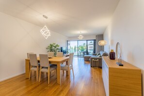 A modern interior with a dining area, a sofa, a TV, and a view through large windows.