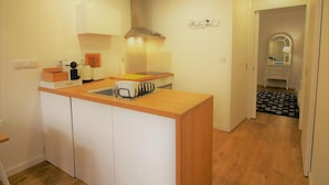 Una cucina compatta con un piano di lavoro in legno, mobili bianchi, un piano cottura integrato e un cartello con la scritta 'Welcome' appeso al muro.