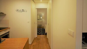 Un corridoio stretto con un bancone di legno a sinistra, un cartello di benvenuto sul muro e un bagno visibile in lontananza.