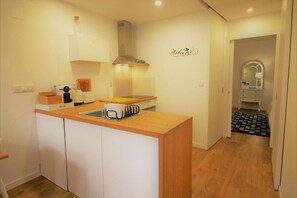 Une cuisine compacte avec un plan de travail en bois, des placards blancs, une cuisinière encastrée et un panneau « Bienvenue » accroché au mur.