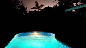 A swimming pool at night with a curved edge and a light source at the far end.