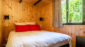 Ein Zimmer mit Holzwandverkleidung, einem Bett, zwei Wandleuchten und einem Fenster mit Blick auf Grünflächen.