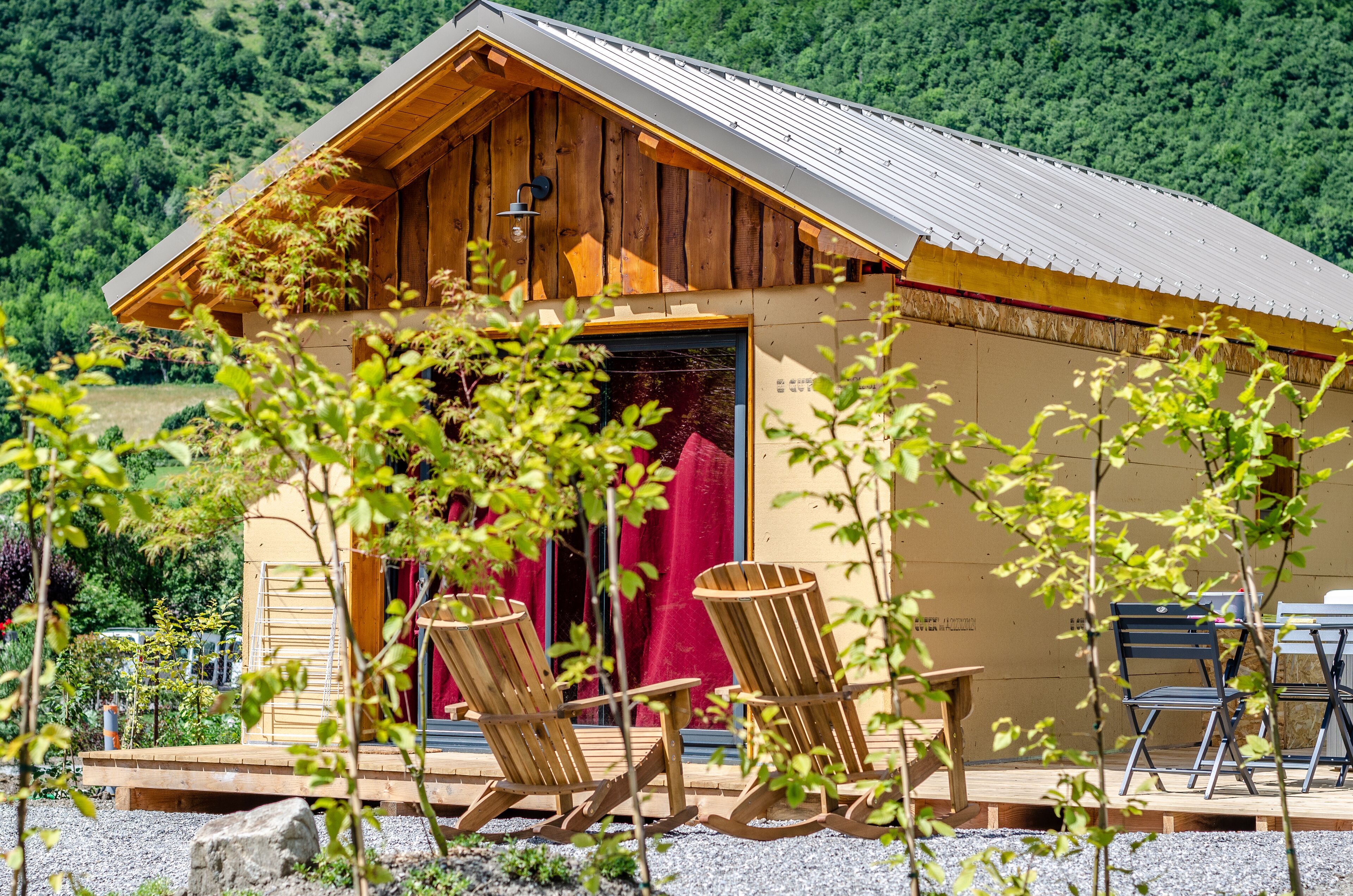 A wooden cabin with a red door, two wooden chairs, and a table outside.