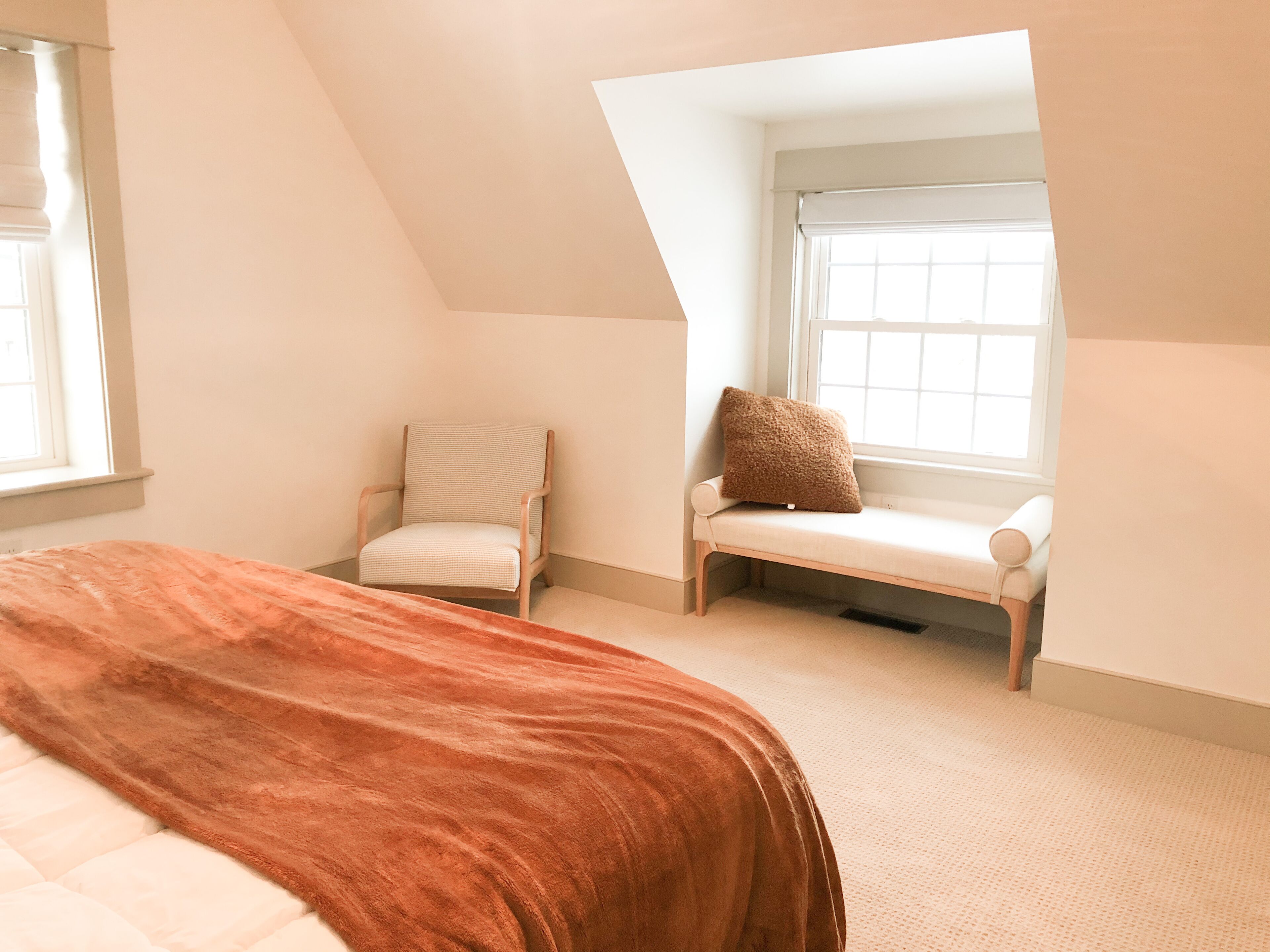 Ein Schlafzimmer mit einem großen Bett, einem Sessel, einem Fenster und einer geneigten Decke.