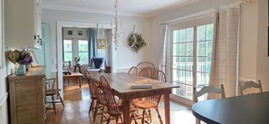 Un comedor con mesa y sillas de madera, una araña y vistas a través de amplios ventanales.