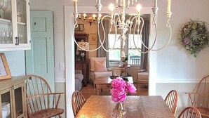 Un comedor con candelabro, sillas de madera, una mesa con un florero y un espejo que refleja la estancia.