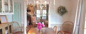 Un coin repas agrémenté d’un lustre, de chaises en bois, d’une table ornée d’un vase de fleurs et d’un miroir qui reflète la pièce.