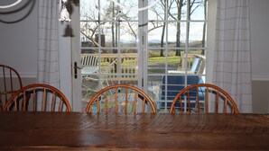Un comedor con mesa y sillas de madera, vista a través de un ventanal hacia una terraza exterior con sillas y una butaca azul.