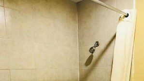 A corner shower with beige tiles, a white bathtub, and a yellow wall. - Roosevelt inn Motel (San Antonio)