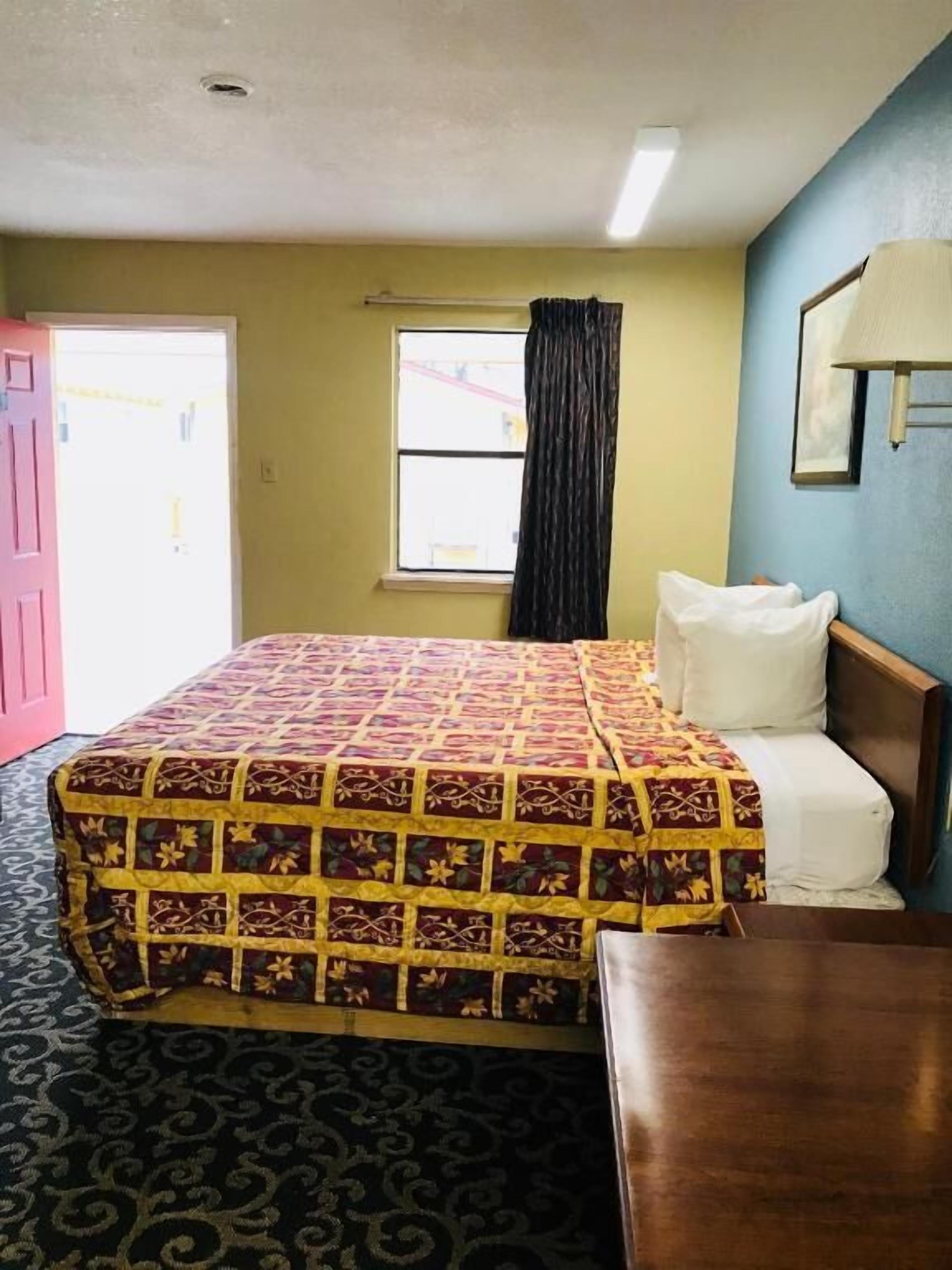 Une chambre d’hôtel avec un lit, une table de chevet, une fenêtre avec des rideaux et une porte.
