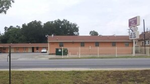 A motel with a simple, single-story structure, a fenced parking area, and a green trash bin. - Roosevelt inn Motel (San Antonio)