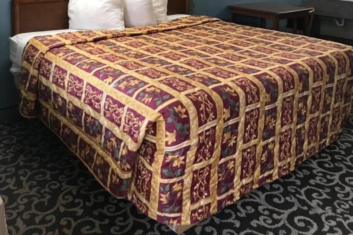 Ein Hotelzimmer mit einem großen Bett, einem Nachttisch, einer Lampe, einem Bild an der Wand und einem Badezimmer mit Spiegel und Handtuchhalter.