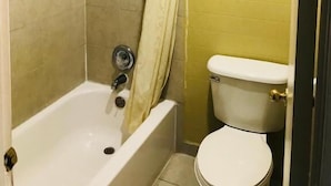 A bathroom with a bathtub, toilet, and shower curtain. - Roosevelt inn Motel (San Antonio)