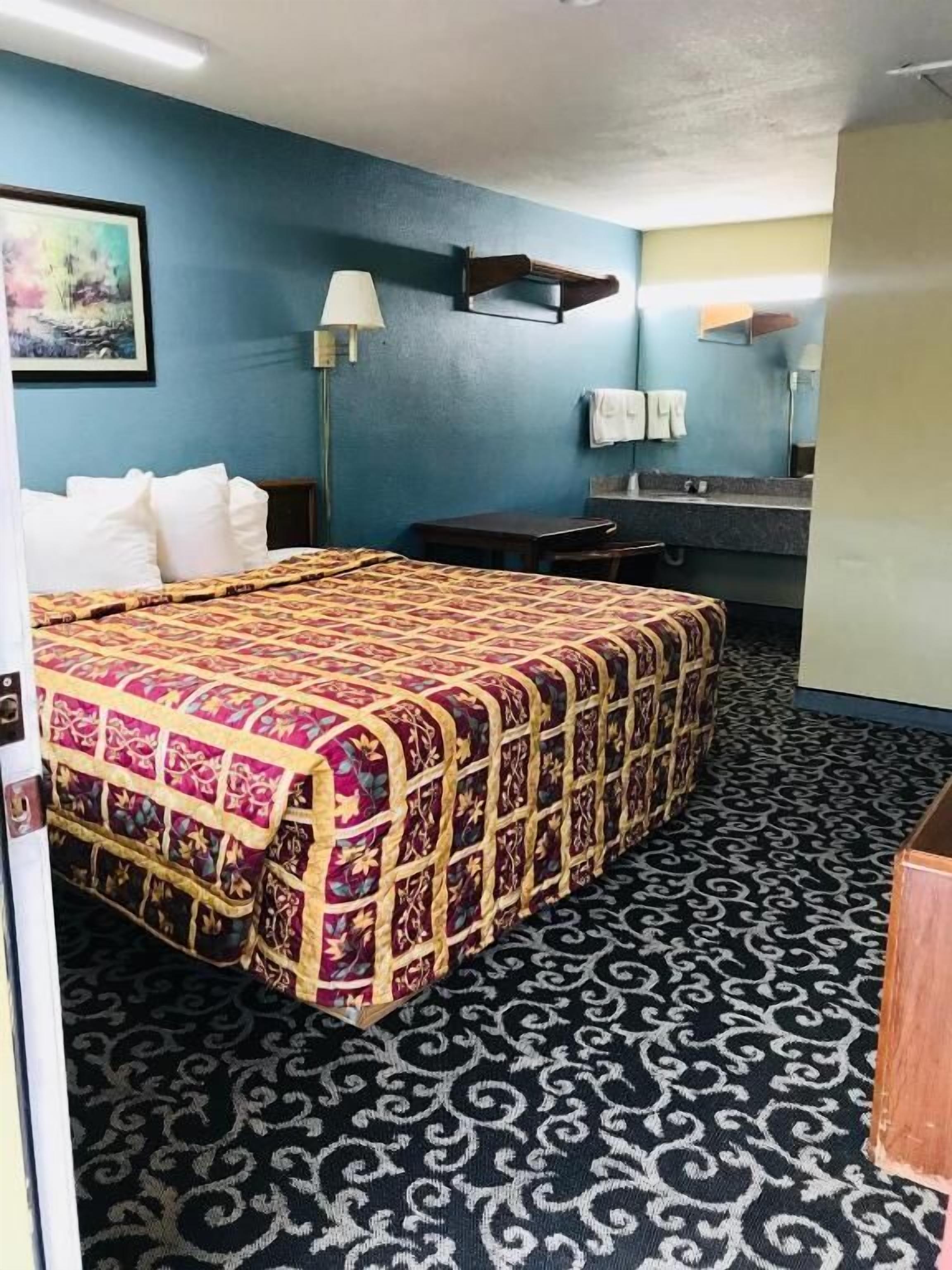 A hotel room with a large bed, a desk, a chair, a mirror, and a bathroom with a sink and towel rack.