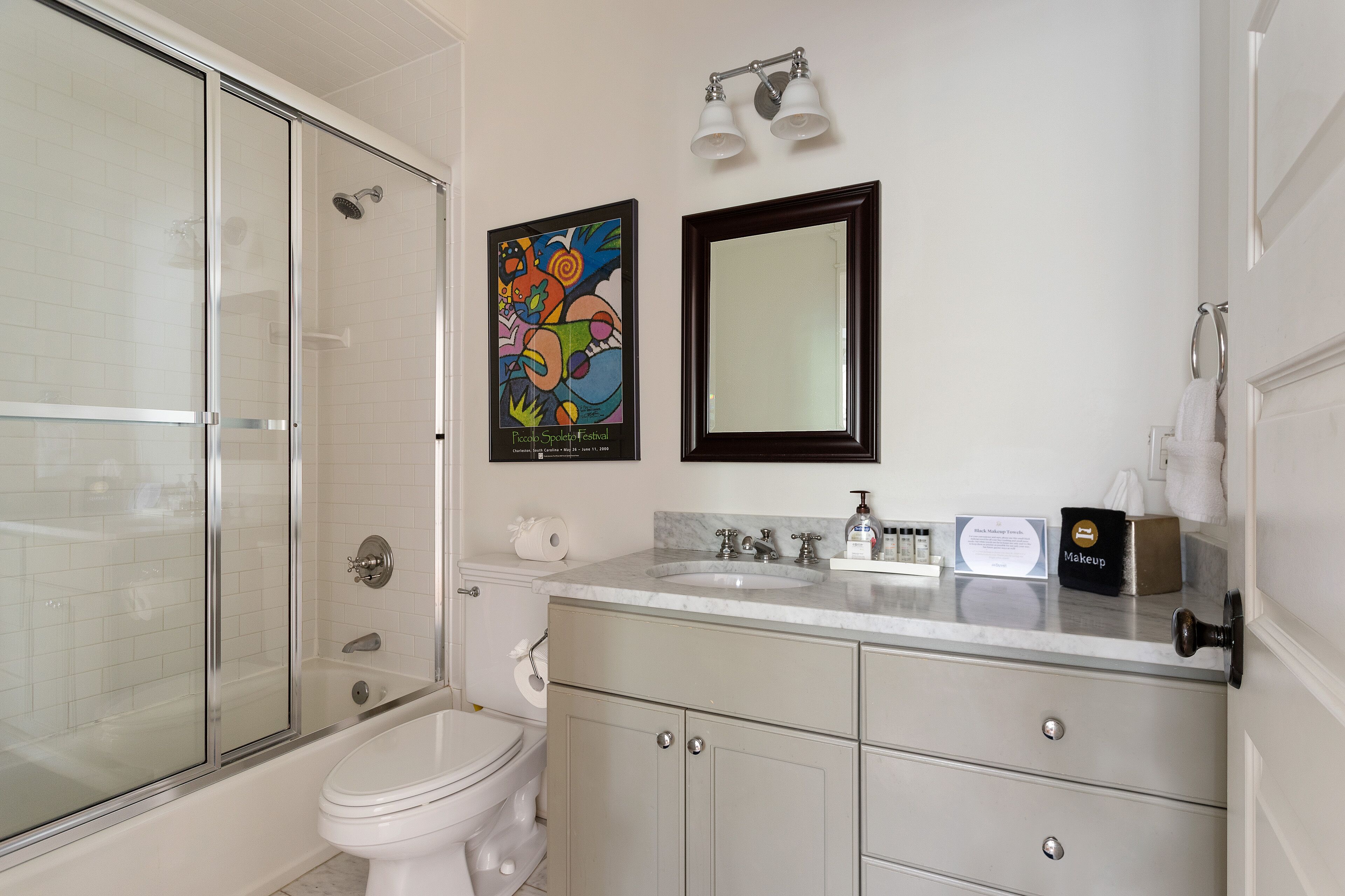 Un baño con cabina de ducha de vidrio, inodoro, lavabo con espejo y una obra de arte enmarcada en la pared.