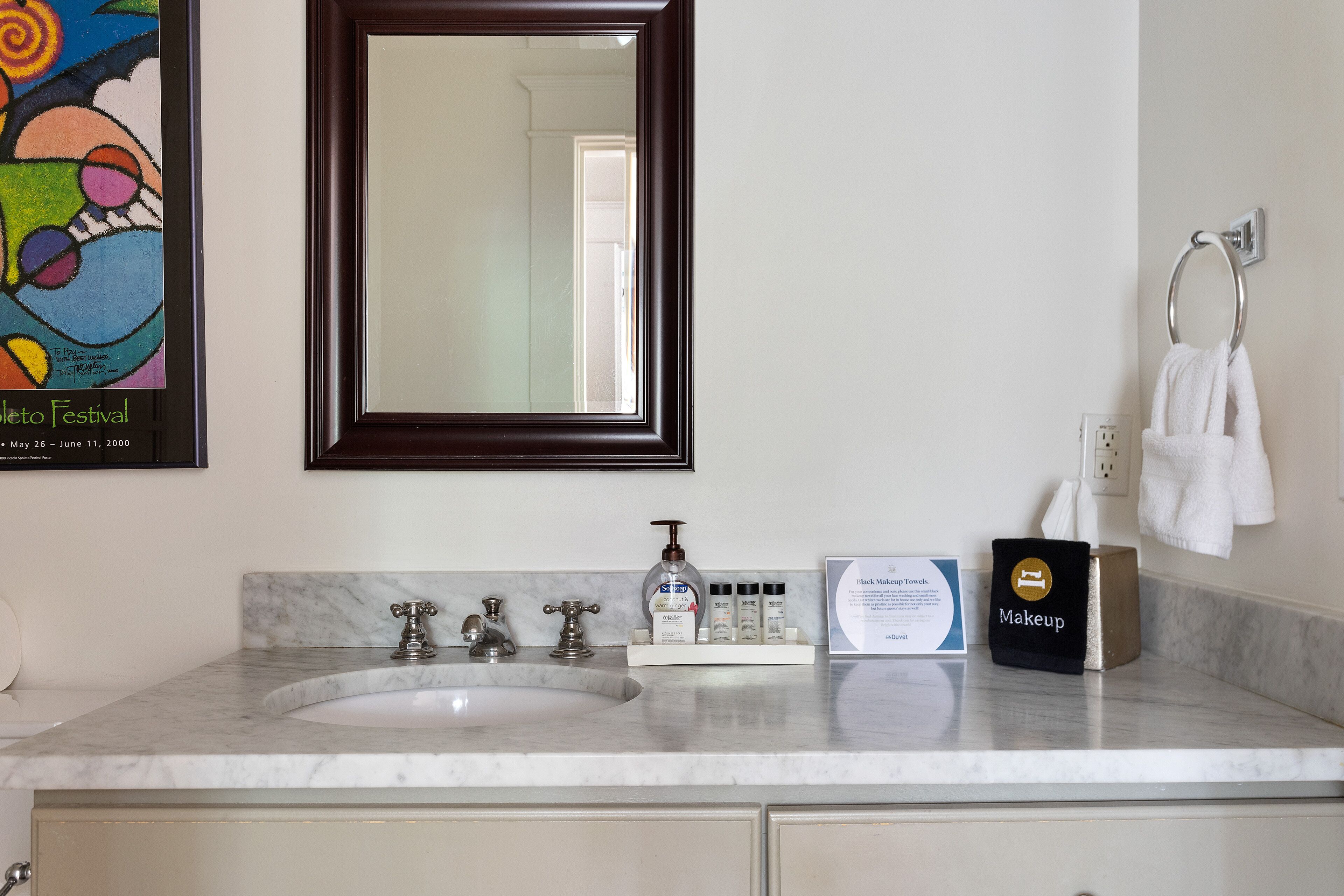 A bathroom with a marble sink, a mirror, a towel rack, and a makeup bag.