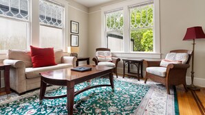 A room with a sofa, armchairs, a coffee table, a patterned rug, and large windows with decorative glass panes.