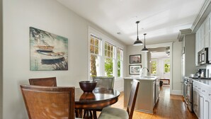 A spacious kitchen with wooden cabinets, a dining area with a round table, and large windows. - Downtown Luxury | The Rainbow Cottage (Charleston)
