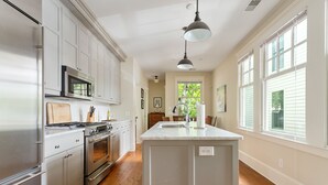 A kitchen with white cabinets, stainless steel appliances, and a large island. - Downtown Luxury | The Rainbow Cottage (Charleston)