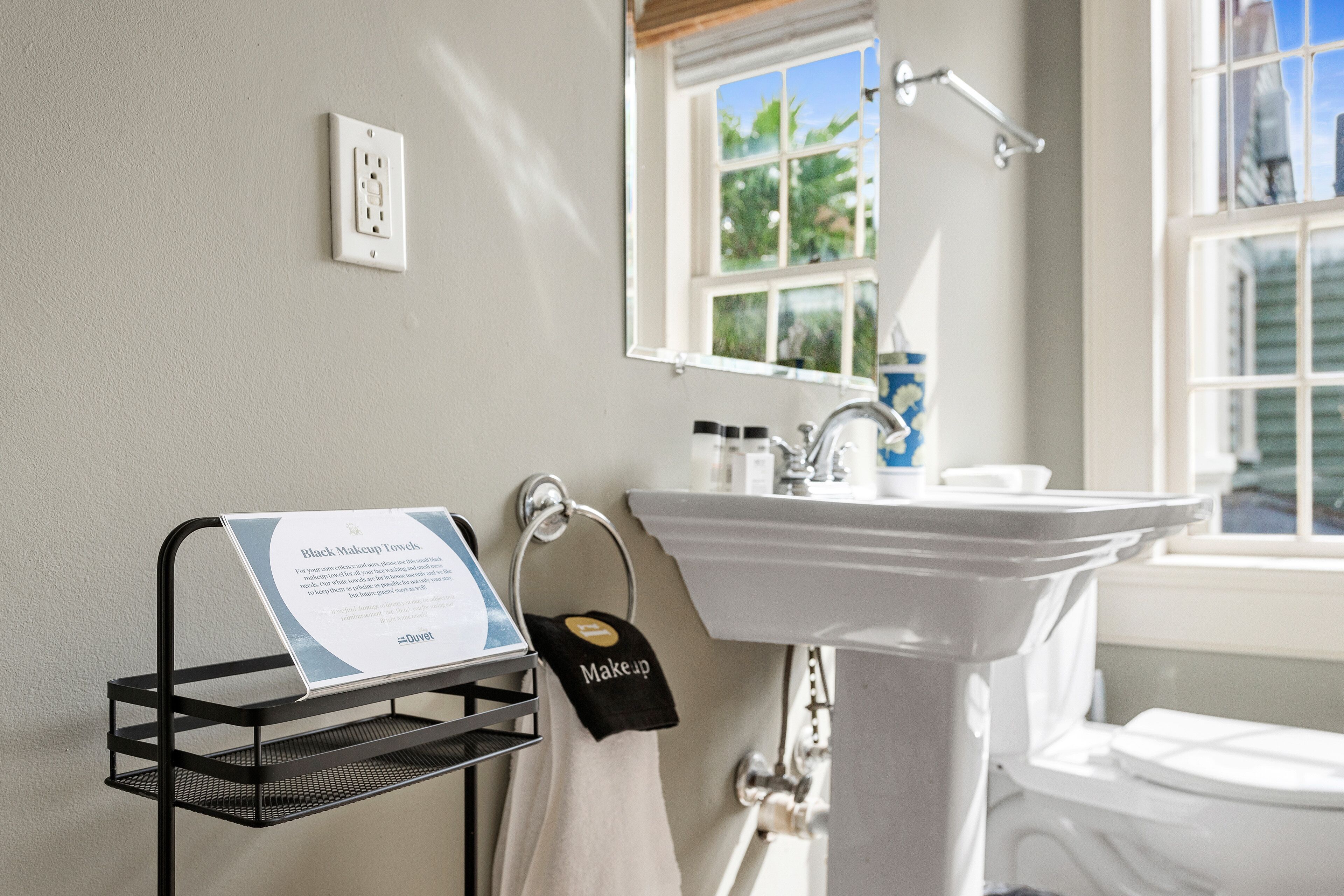 A bathroom with a white sink, a mirror, and a black towel rack with a sign.