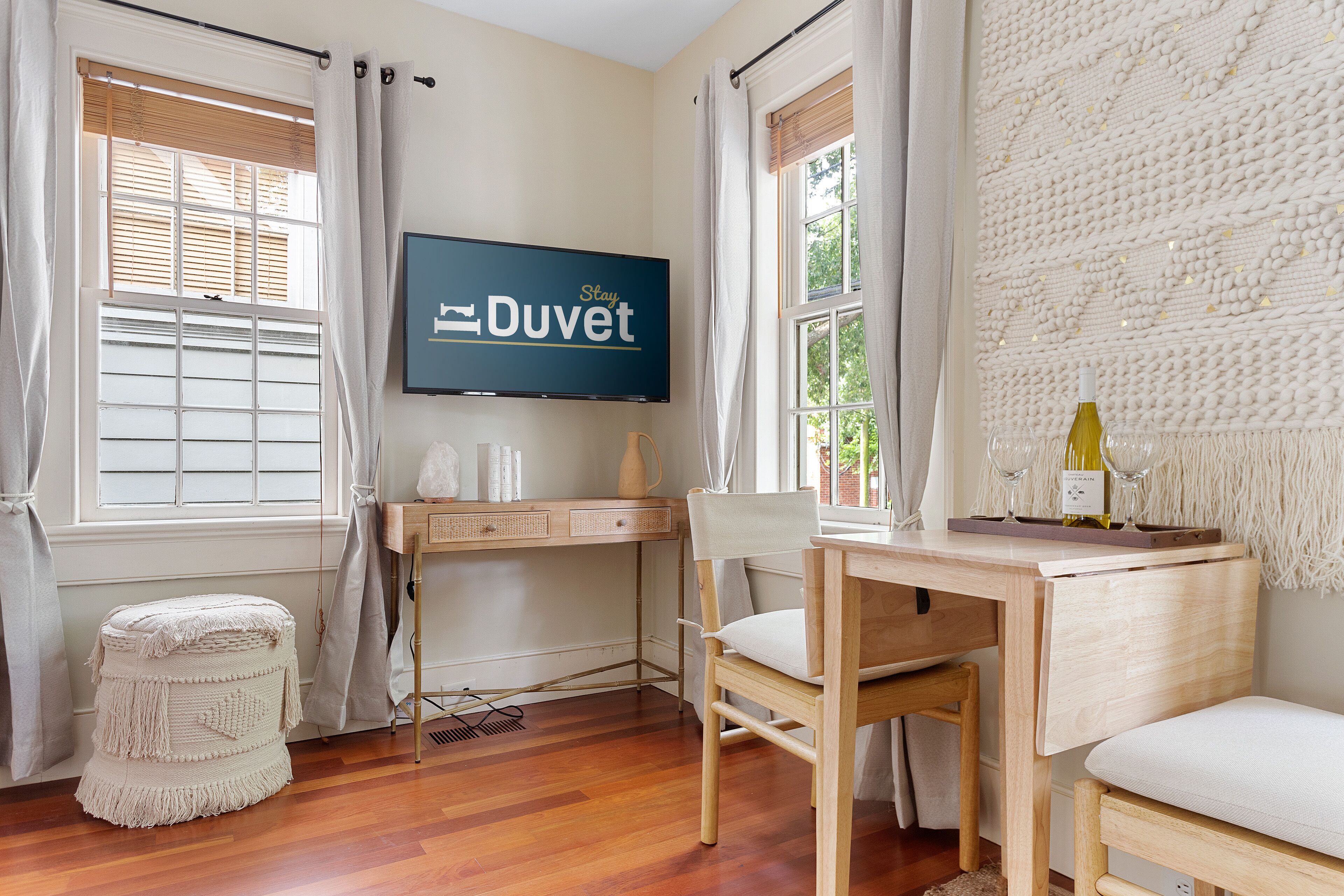 Ein Zimmer mit einem Holztisch, einem Stuhl, einem Fernseher und einem Fenster mit Blick auf Bäume.
