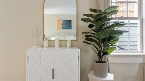 Un mueble blanco con una superficie espejada, una planta en maceta y una ventana con persianas.