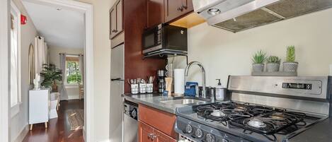 A kitchen with wooden cabinets, a stainless steel range hood, a gas stove, and a microwave.