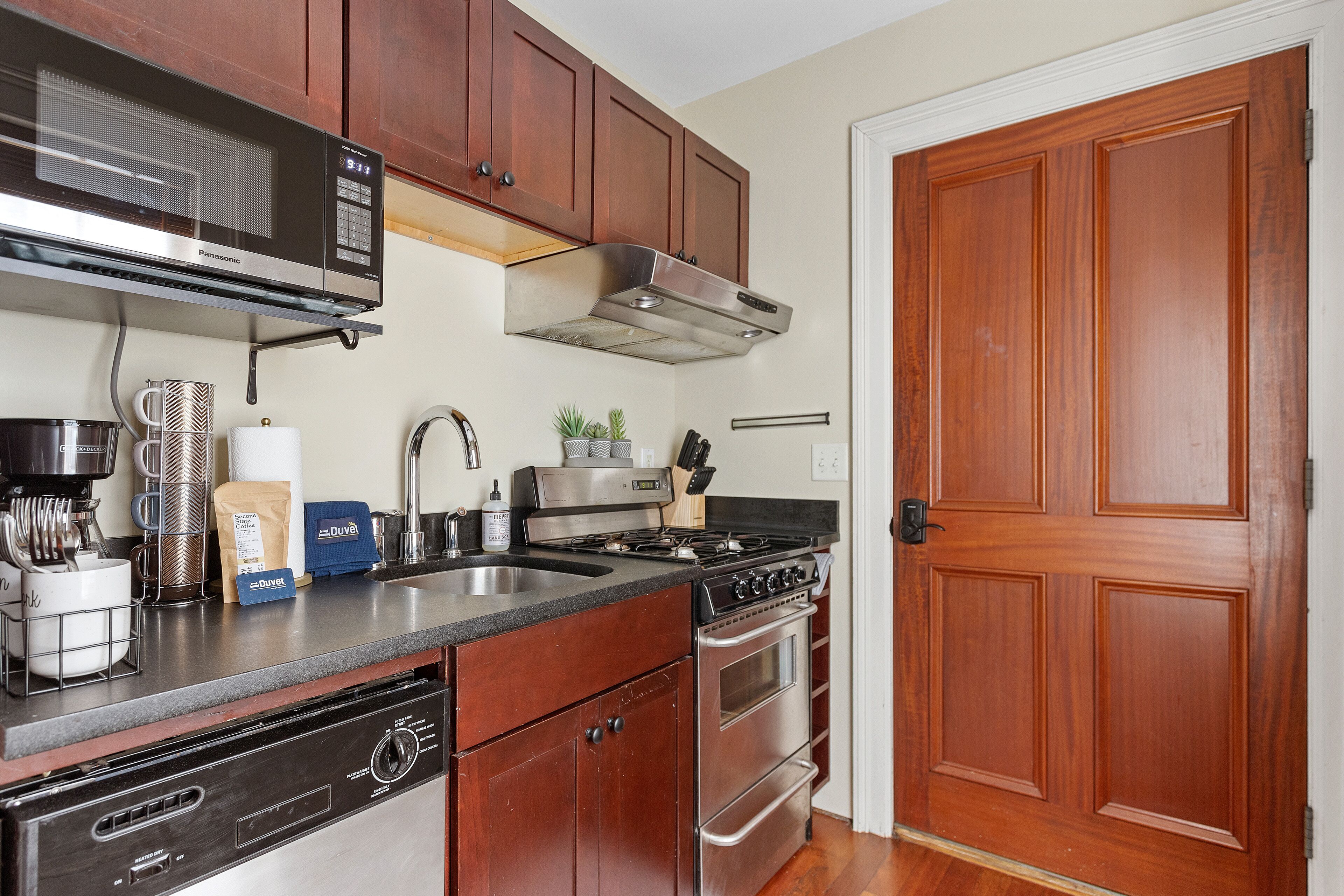 Una cocina con armarios de madera, estufa de acero inoxidable, microondas y lavavajillas.